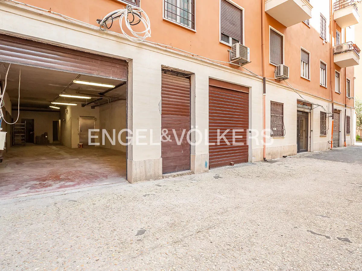 Exterior view of a building with brown garage doors, one open, revealing a large, empty space with fluorescent lights.