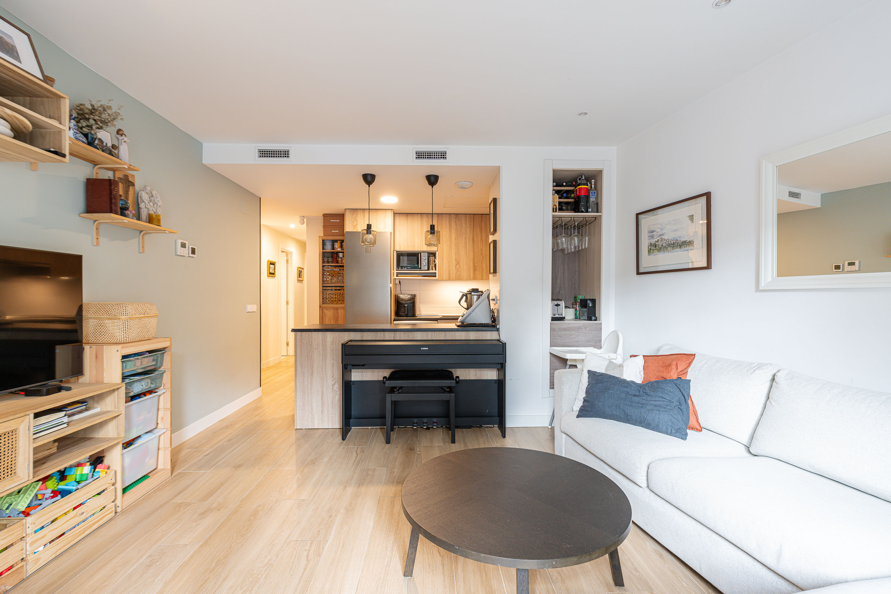 Modern living room with a white sofa, round coffee table, and a piano positioned against a kitchen island with wood cabinets. [AI-generated text]