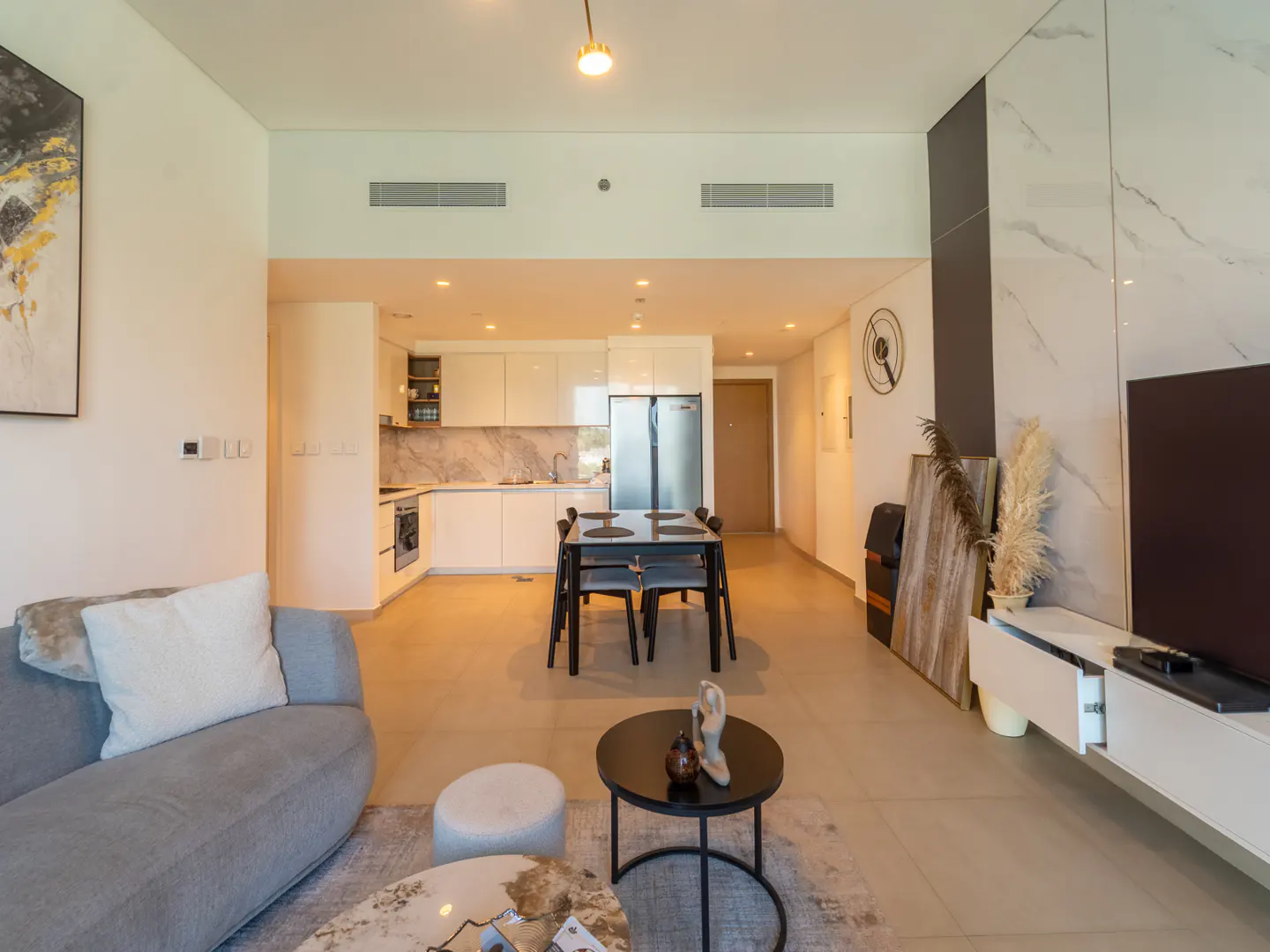 A modern apartment interior with a gray sofa, open kitchen, dining table, and neutral decor.