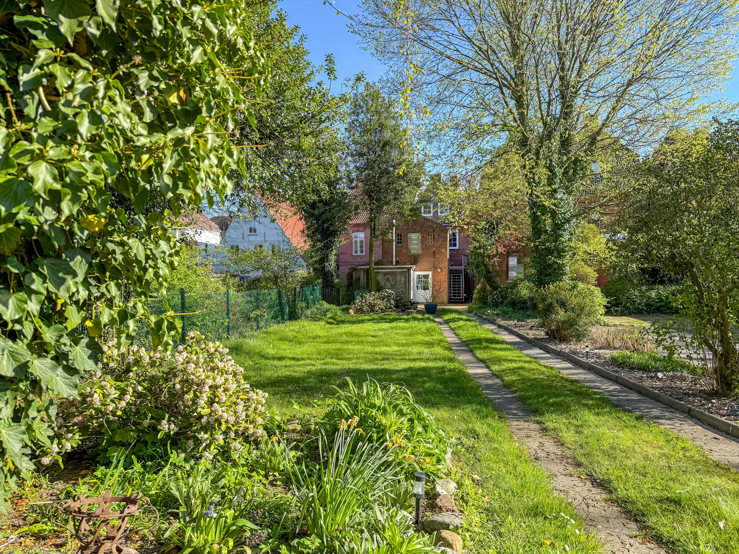 A long green lawn leads to a red brick house with a white door, framed by trees and lush greenery.