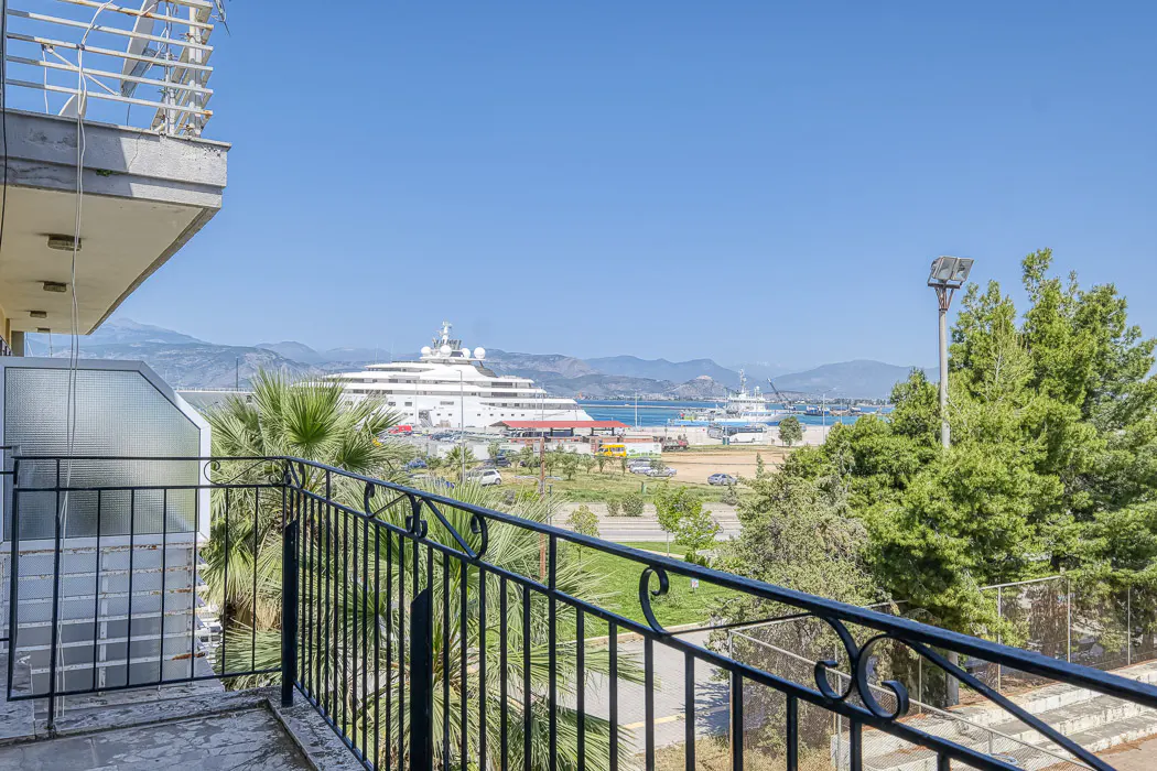 View from a balcony with black railings overlooking a harbor with a large white yacht and mountains in the background.