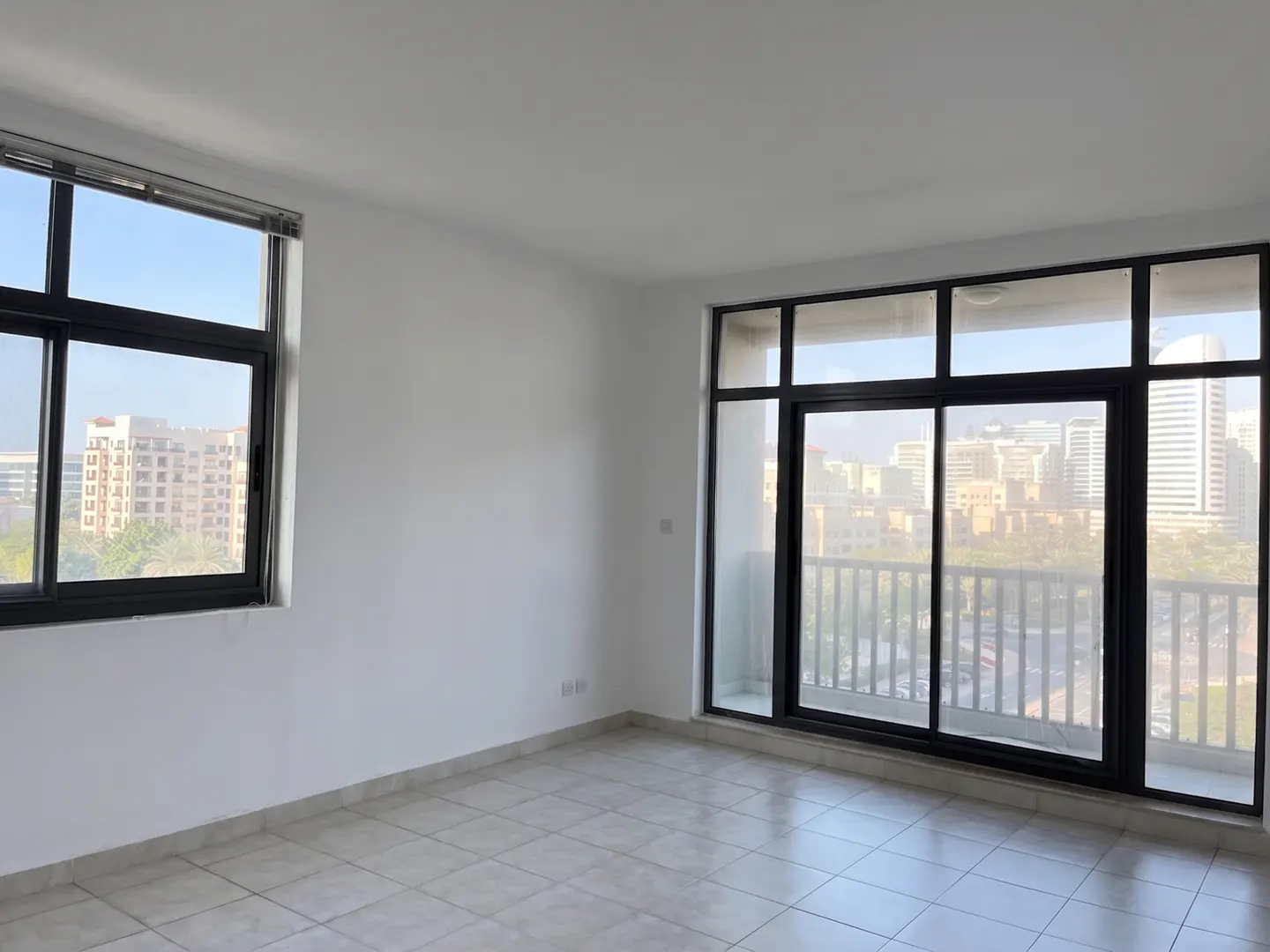 Empty room with white walls, tiled floor, and black-framed windows overlooking a cityscape.