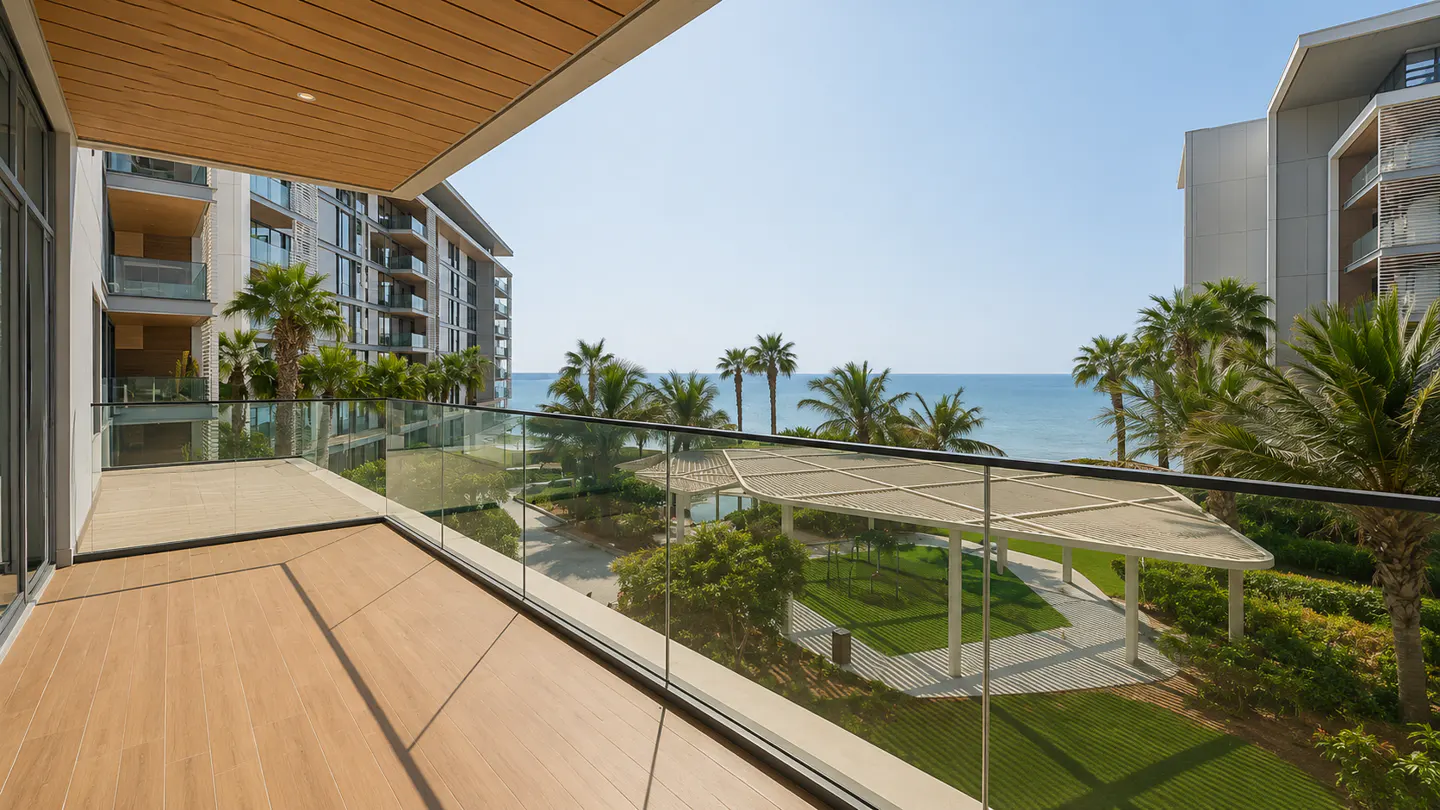 Balcony view of ocean, palm trees, and modern buildings. Wood-look flooring and glass railing. Blue sky.