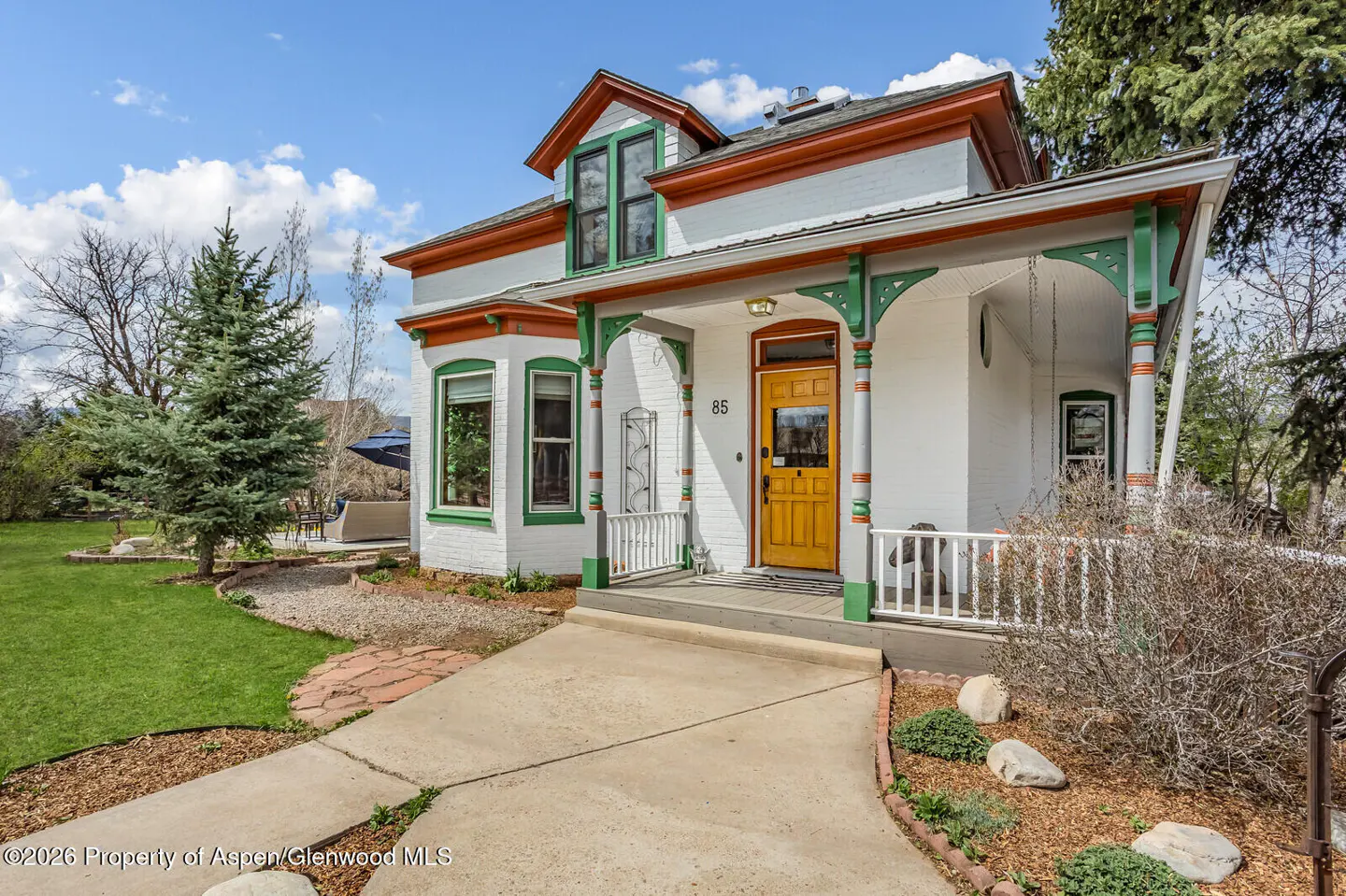 Exterior of a white house with green and orange trim, a yellow door, and a concrete walkway.