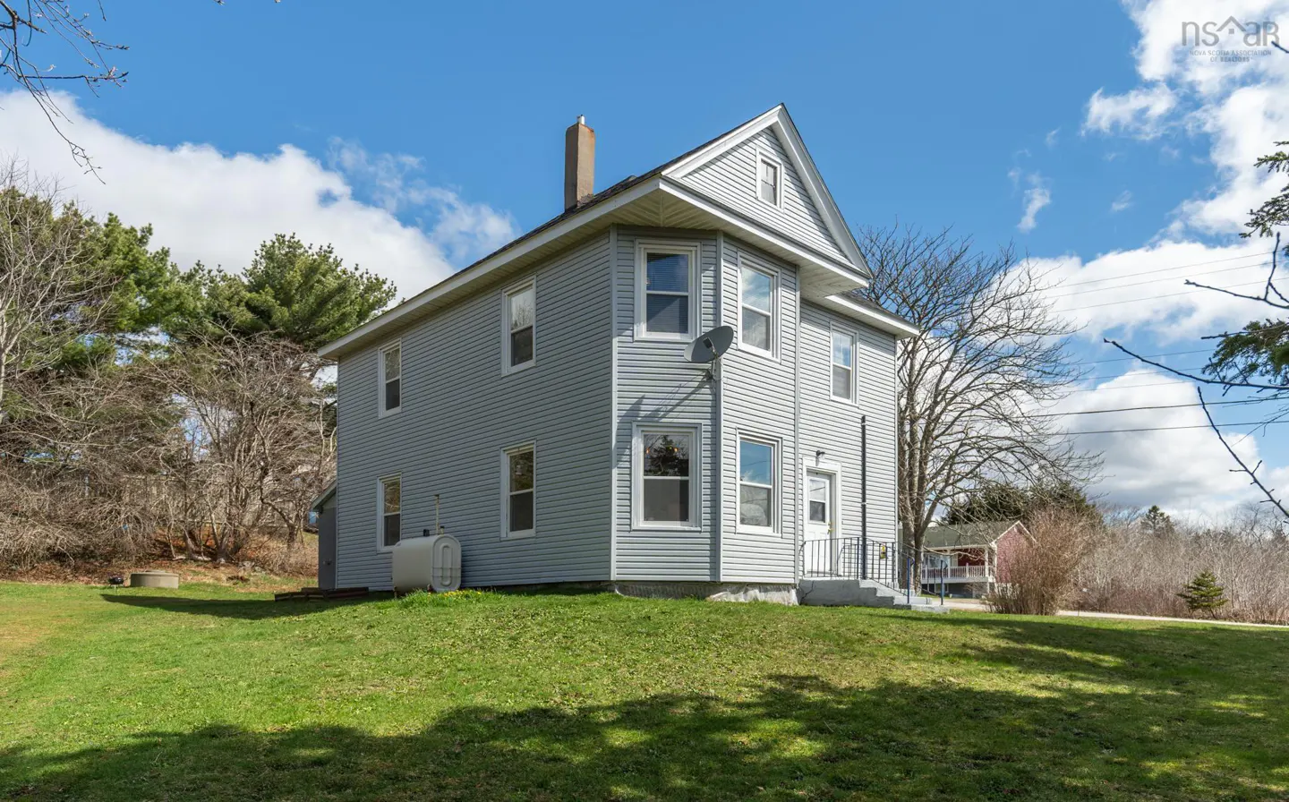 Two-story gray house with white trim, a chimney, and a satellite dish on a green lawn under a blue sky.