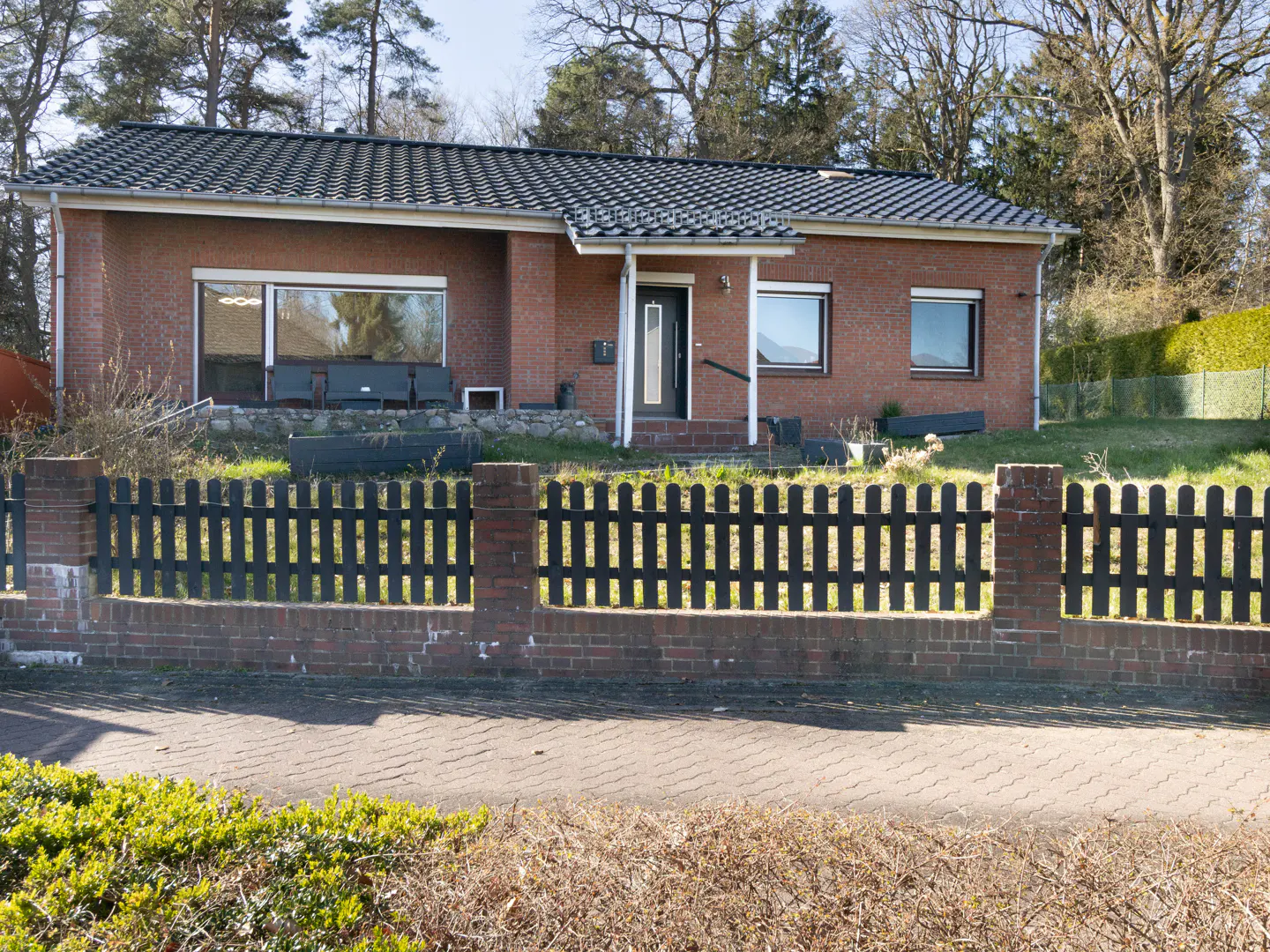 A single-story red brick house with a black roof and a black picket fence.