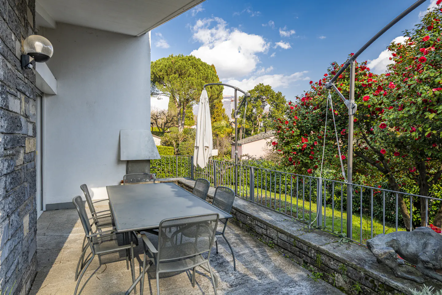 Outdoor patio with a gray table and chairs, stone wall, and a view of trees and blue sky.