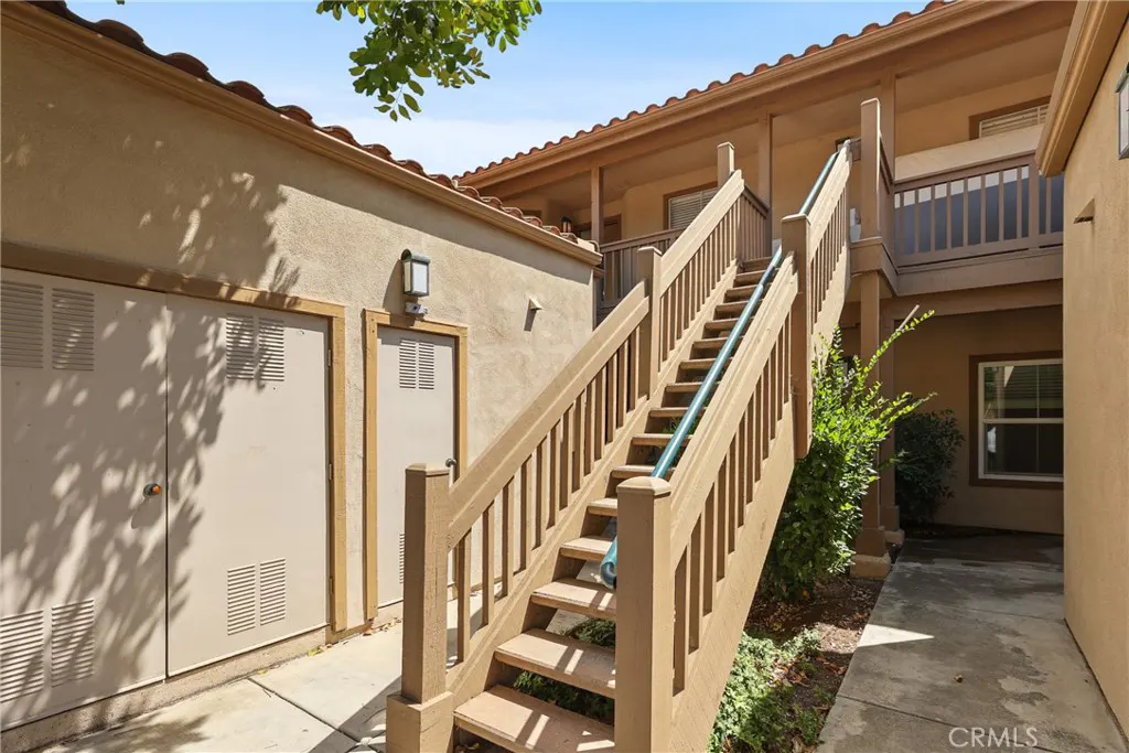 Exterior view of a two-story tan apartment building with a wooden staircase leading to the second floor.