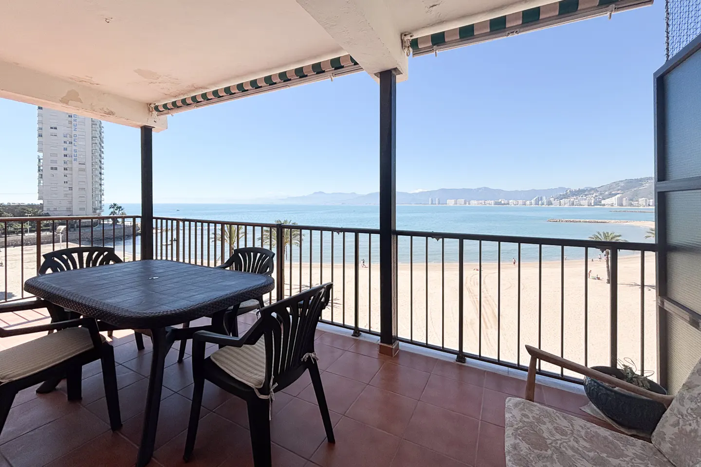 Balcony view of a beach with a table and chairs. The ocean is blue and the sky is clear.