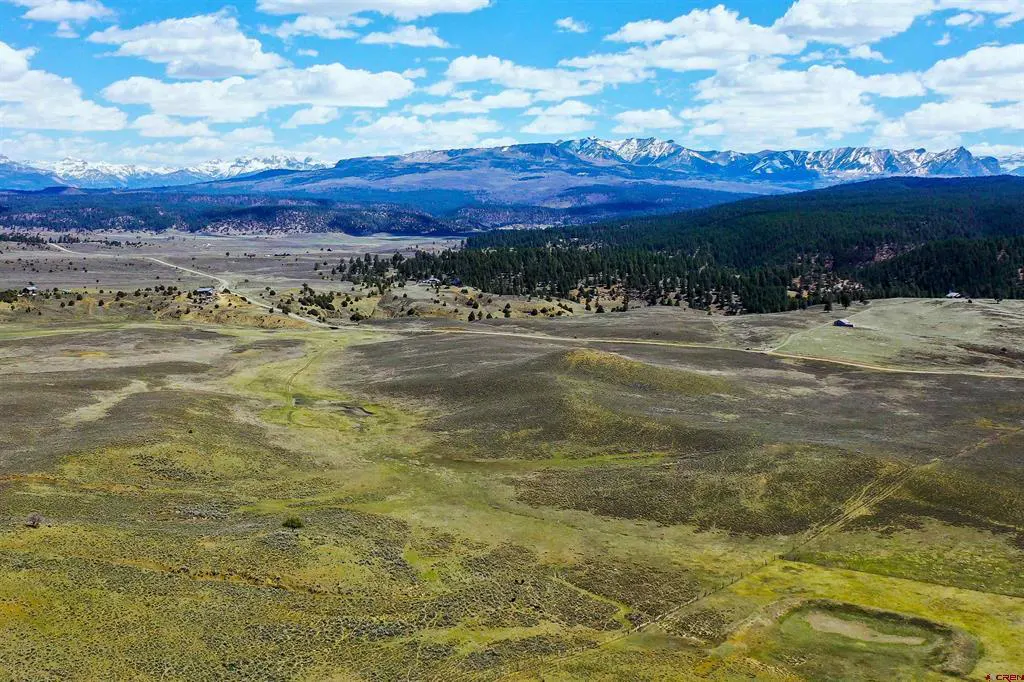 Scenic view of a green and brown valley with snow-capped mountains in the background under a blue sky with white clouds.