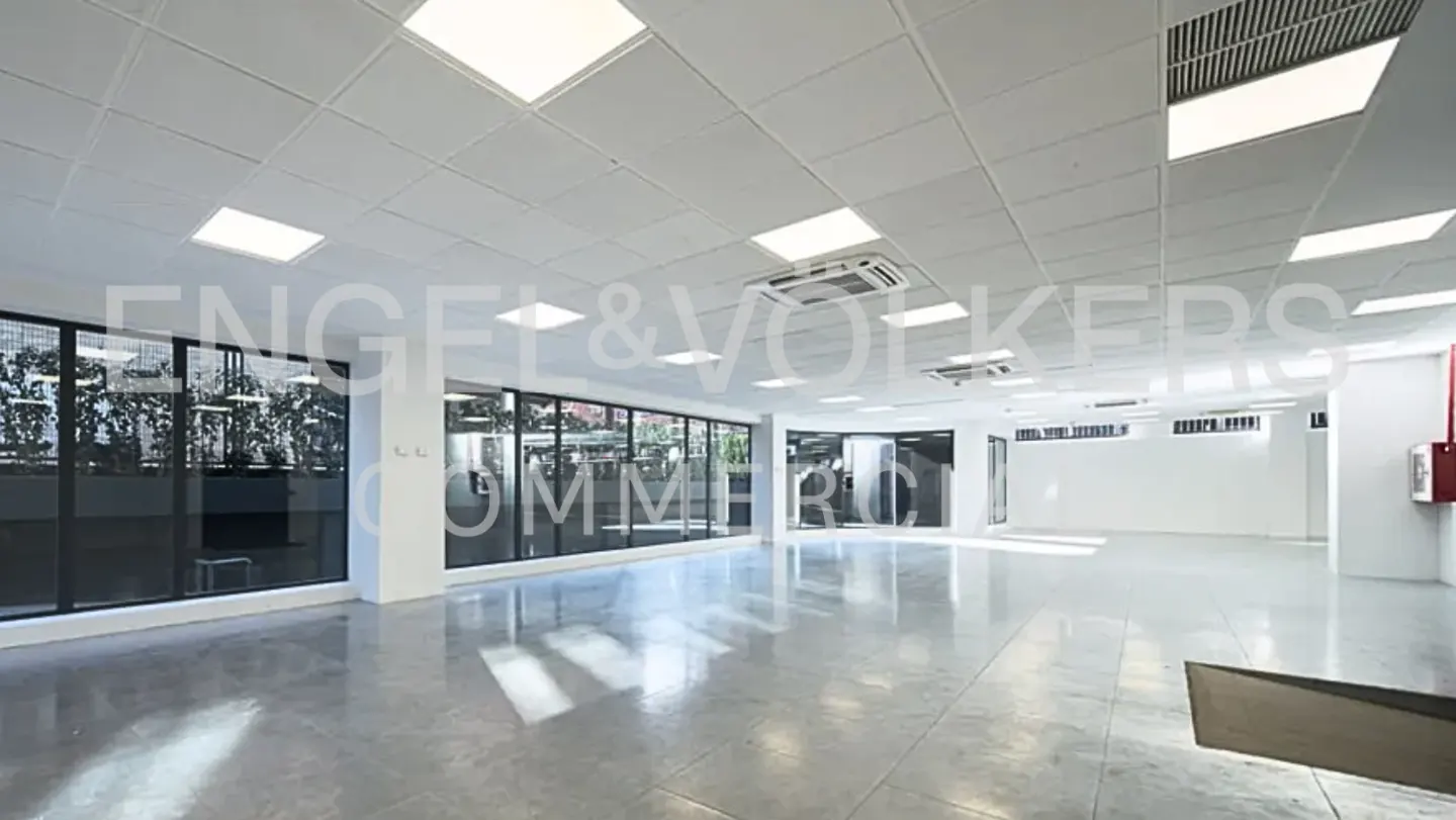 Bright, empty commercial space with large windows, white walls, and a tiled ceiling with recessed lighting. Engel & Volkers logo visible.