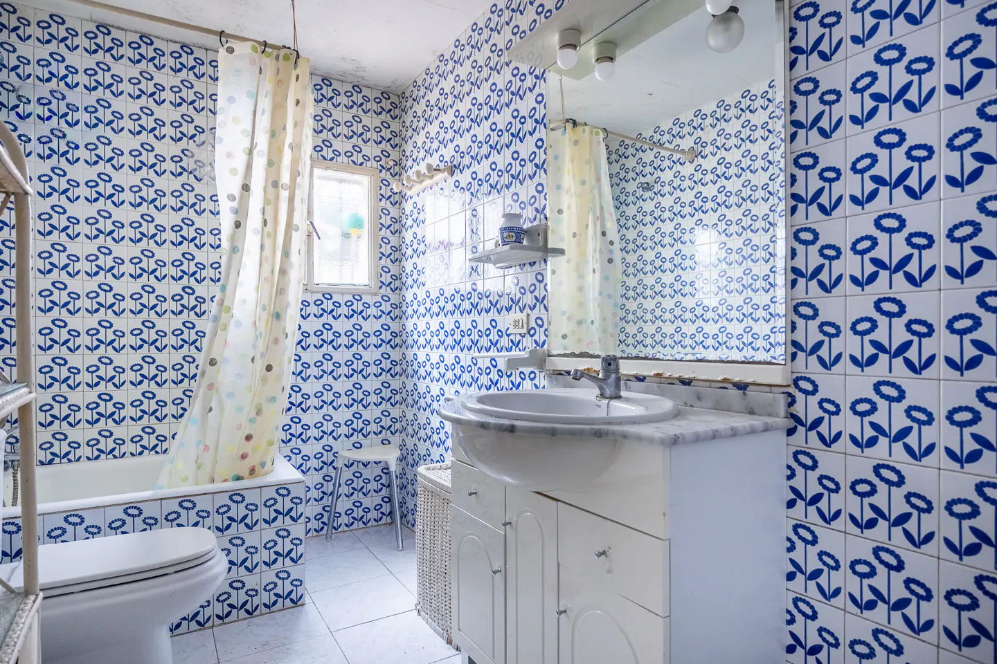 Bathroom with blue flower tile, white sink vanity, toilet, and tub with shower curtain.