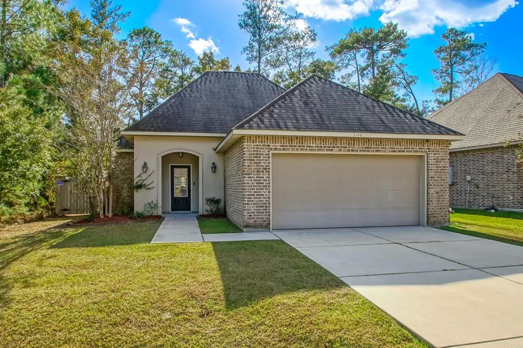 A single-story brick house with a gray roof, a two-car garage, and a green lawn on a sunny day.
