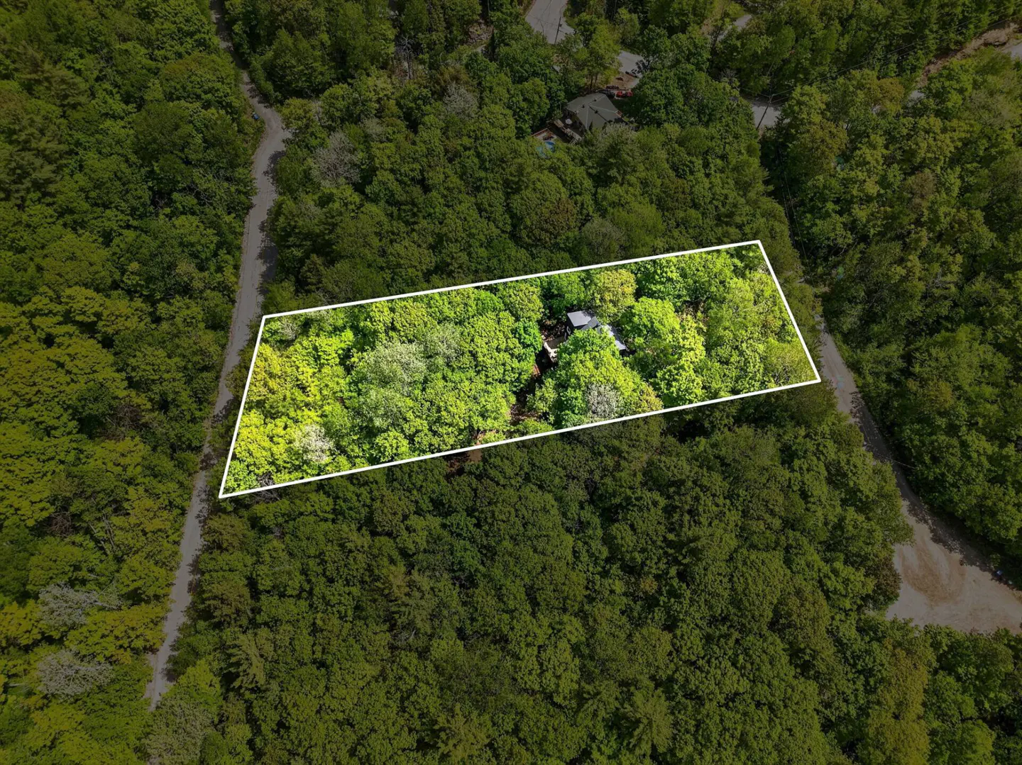Aerial view of a wooded lot outlined in white, nestled within a dense forest near a winding road.
