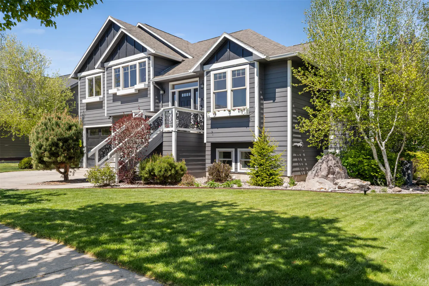 Two-story gray house with white trim, a staircase to the front door, and a green lawn.