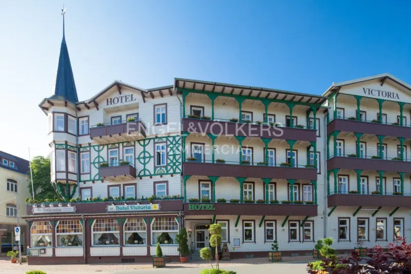 Exterior of Hotel Victoria, a multi-story white building with green trim and balconies, under a clear blue sky.