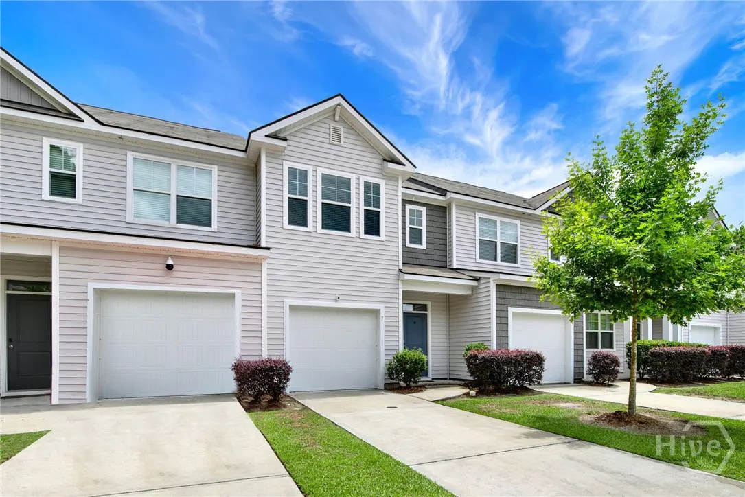 Exterior view of gray townhouses with white garage doors, green grass, and a blue sky.