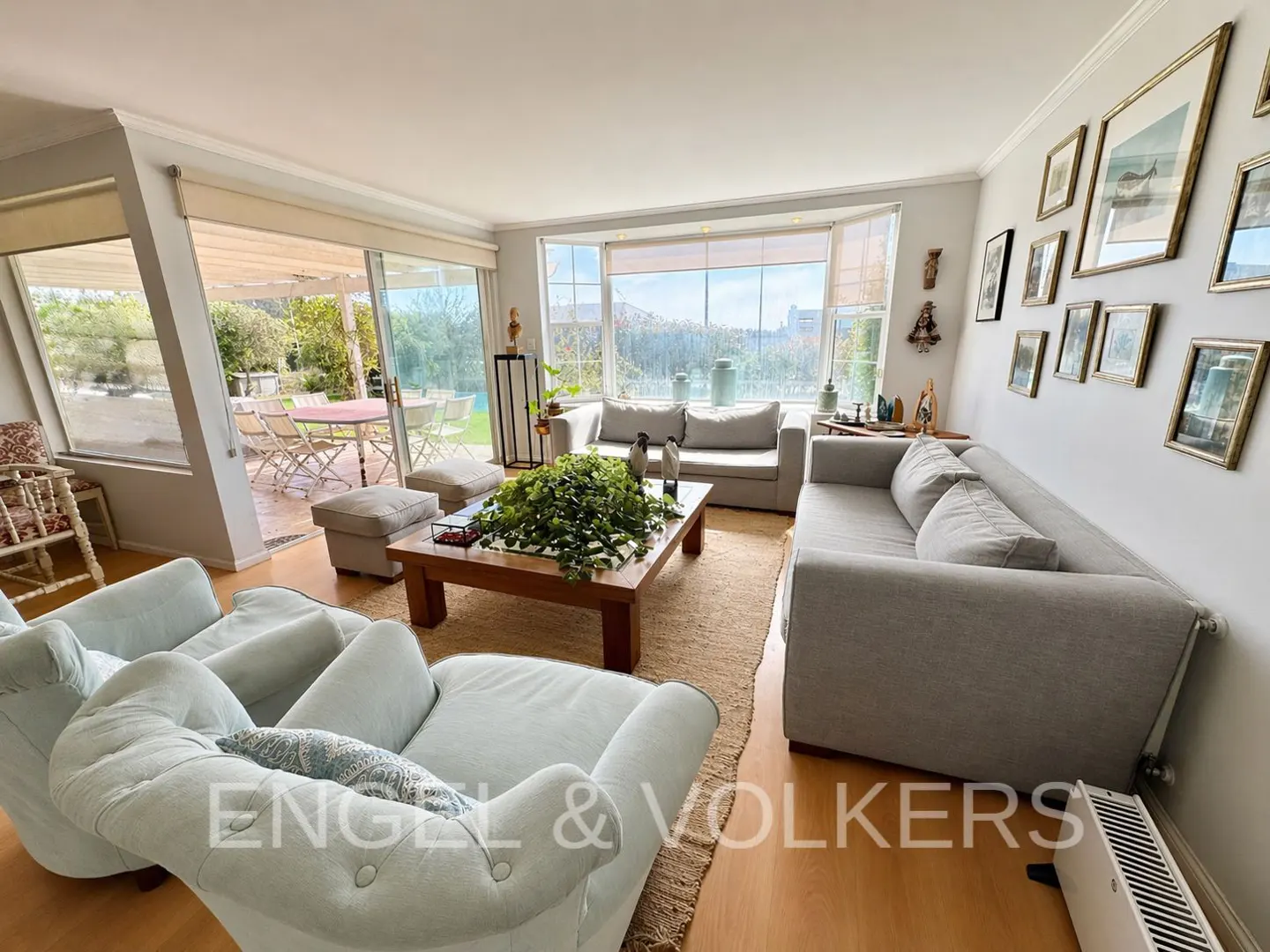 Living room with light blue armchairs, gray sofas, wood floors, and a view of a patio with a table and chairs.