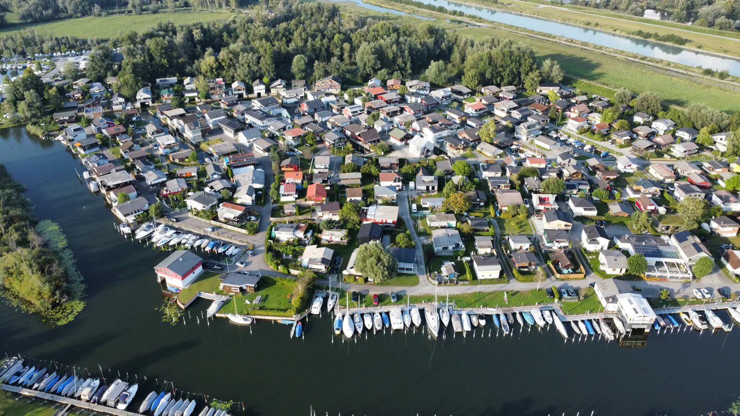 Aerial view of a dense waterfront community with houses, boats, and green trees.