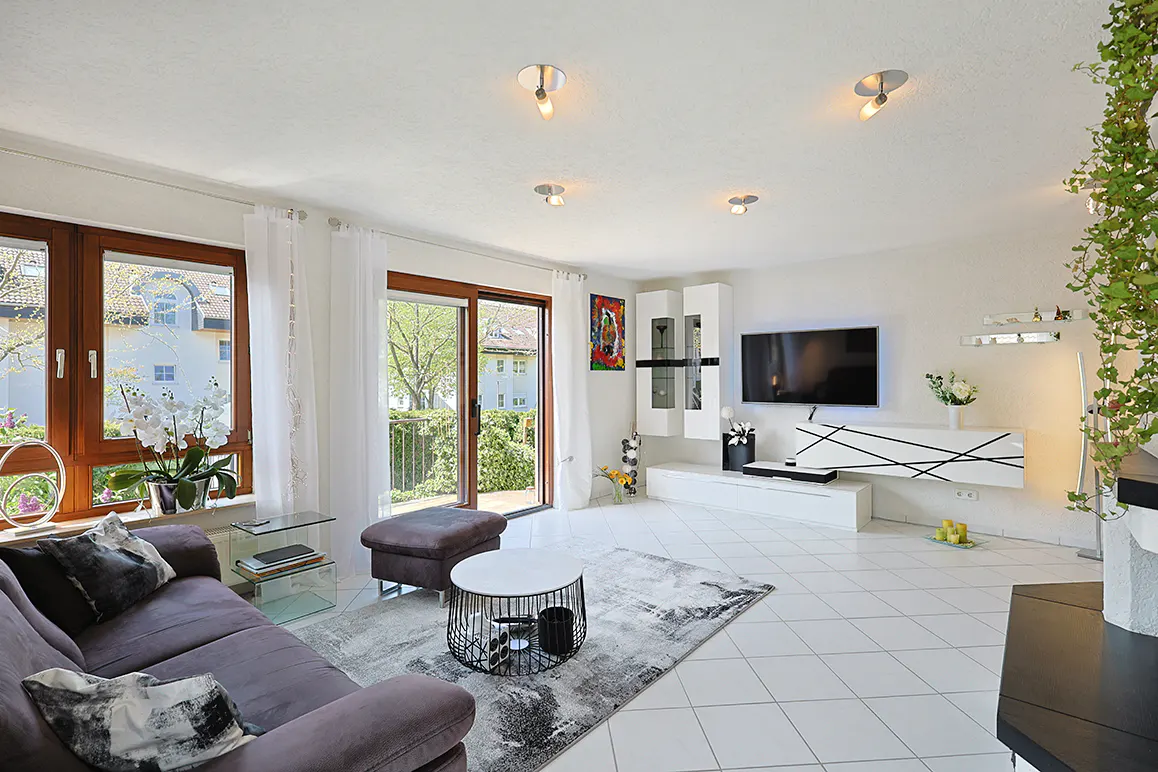 Bright living room with a brown sofa, white tile floor, and a sliding glass door to a balcony. A modern entertainment center is on the right wall.