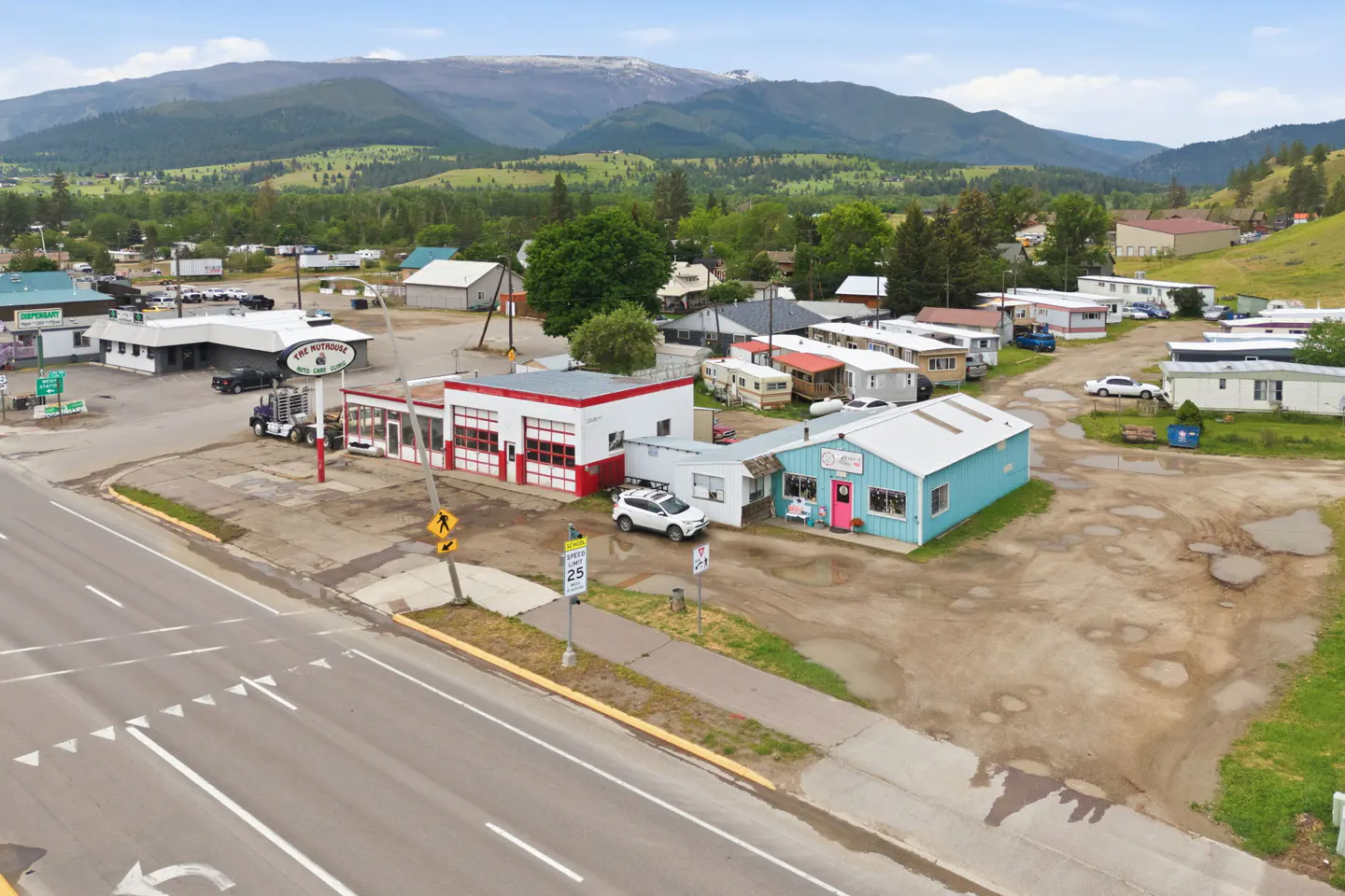 Aerial view of a commercial property with a red-and-white garage and blue building near a road, set against mountains.