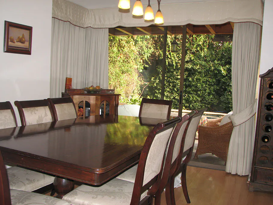 Dining room with a dark wood table and chairs, light walls, and a view of lush greenery through a sliding glass door.