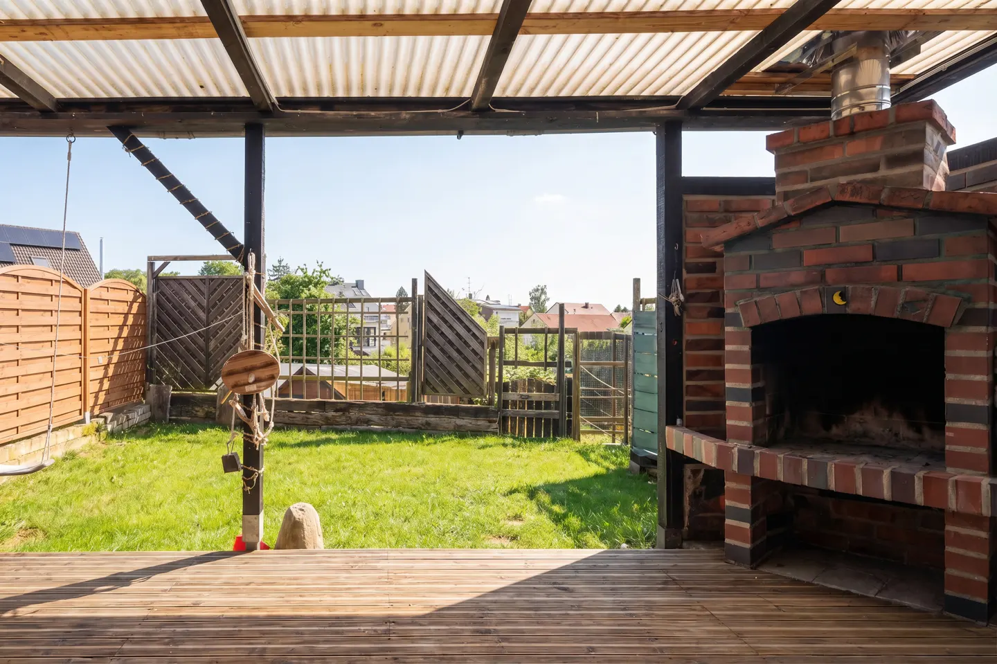 Covered patio with wood deck, brick fireplace, and green lawn. A swing set is visible in the background.