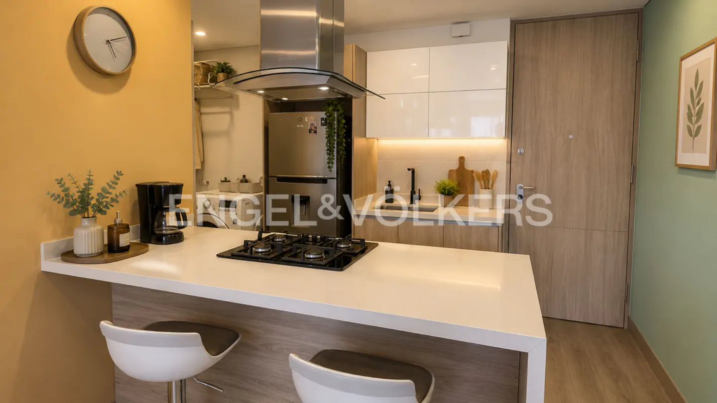 A modern kitchen with a white countertop island, stainless steel appliances, and light wood cabinets. Two white bar stools are in the foreground.