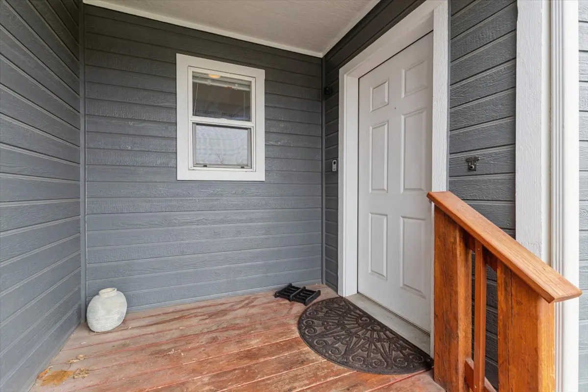 Front porch with gray siding, white door and trim, and a small window. A wooden railing is on the right.