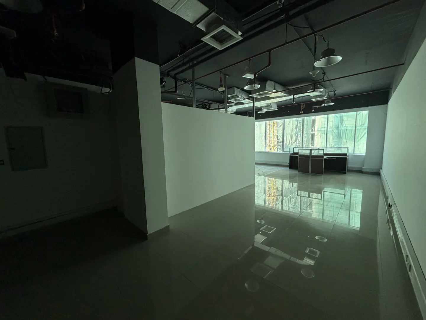Empty office space with a black ceiling, white walls, and a shiny gray floor. Desks are visible by the window.