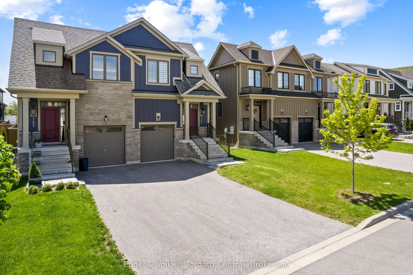 Row of modern townhouses with blue, brown, and white exteriors, each with a garage and front steps, under a partly cloudy sky.