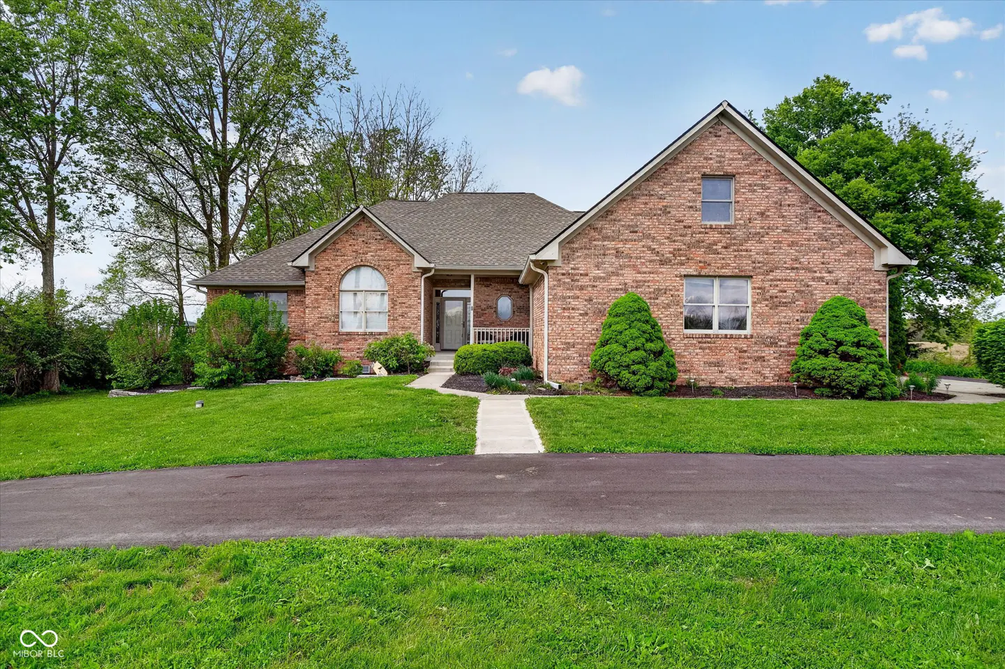 A single-story brick house with a gray roof, green lawn, and black driveway.