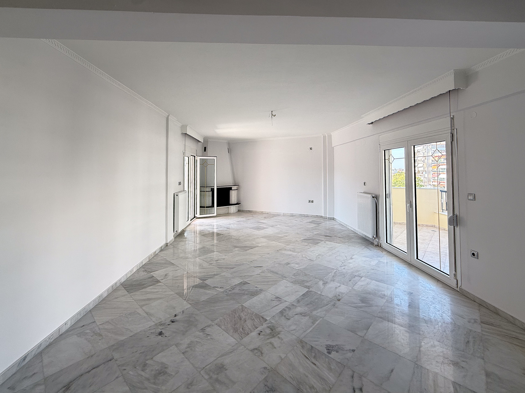 Spacious, empty living room with white walls, marble tile floors, a corner fireplace, and glass doors leading to a balcony. [AI-generated text]