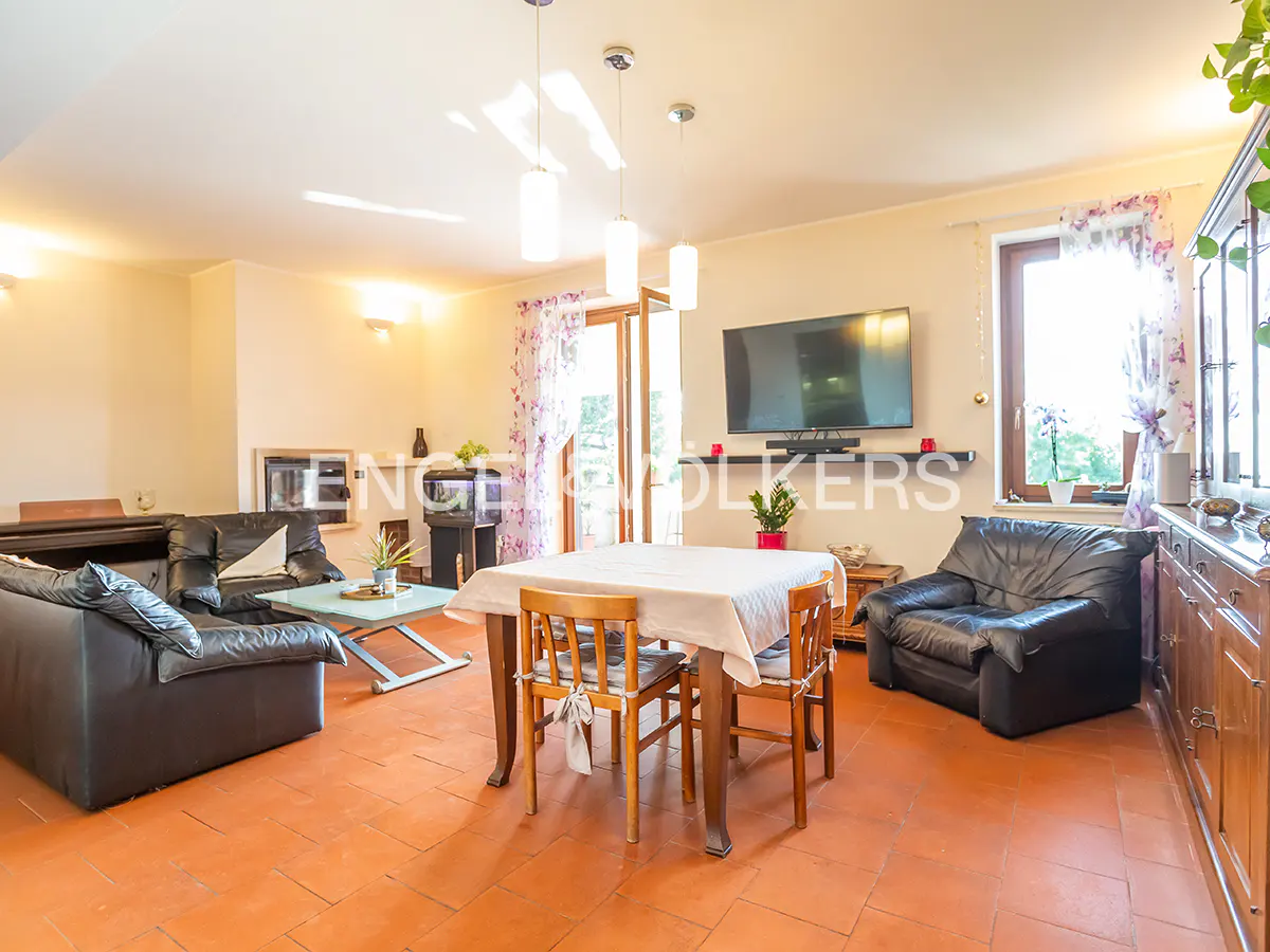 Living room with terracotta tile floor, black leather sofas, and a dining table with a white tablecloth. A TV hangs on the wall.