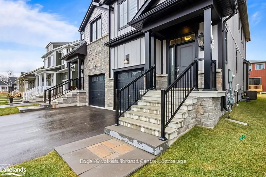 Exterior view of a two-story house with gray siding, stone accents, and a black front door with stairs.