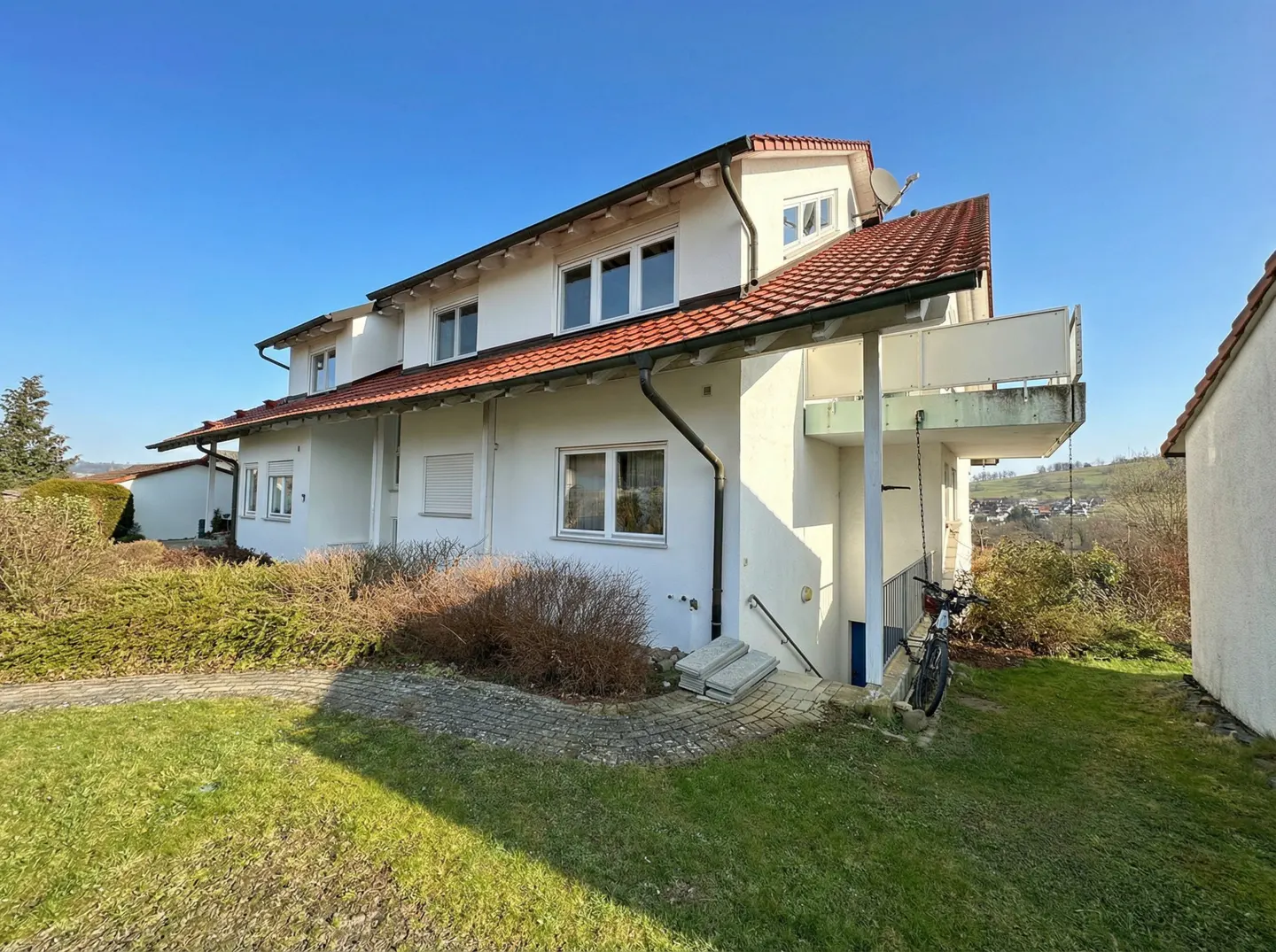 Exterior view of a two-story white building with a red tile roof, a balcony, and a green lawn on a sunny day.