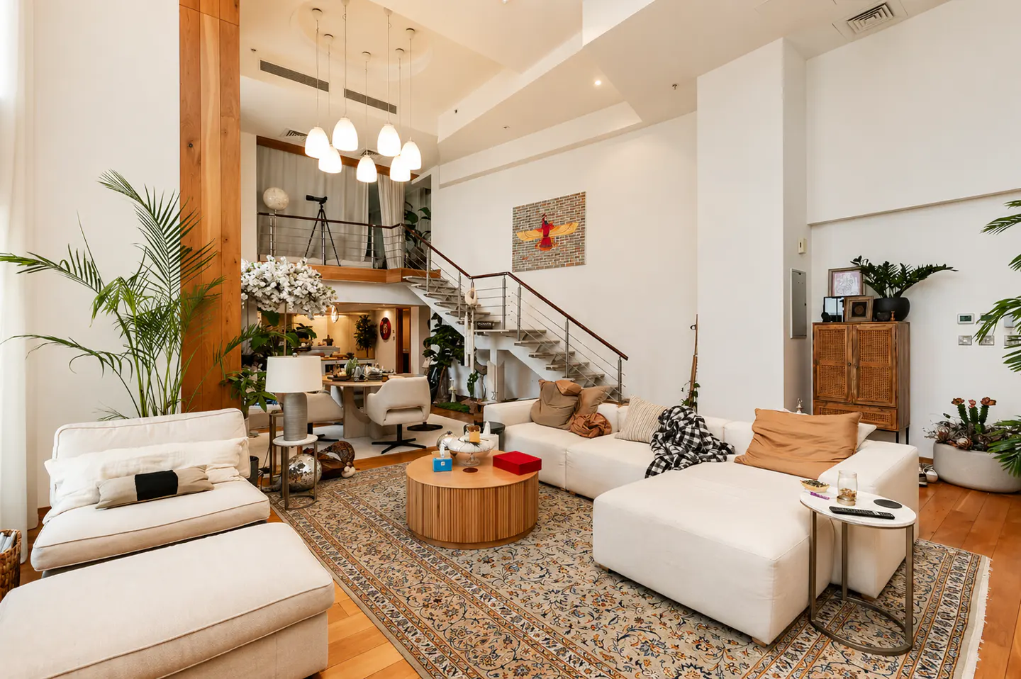 Bright, open living room with white sectional sofa, wood floors, and a staircase leading to a loft area. A patterned rug adds warmth.