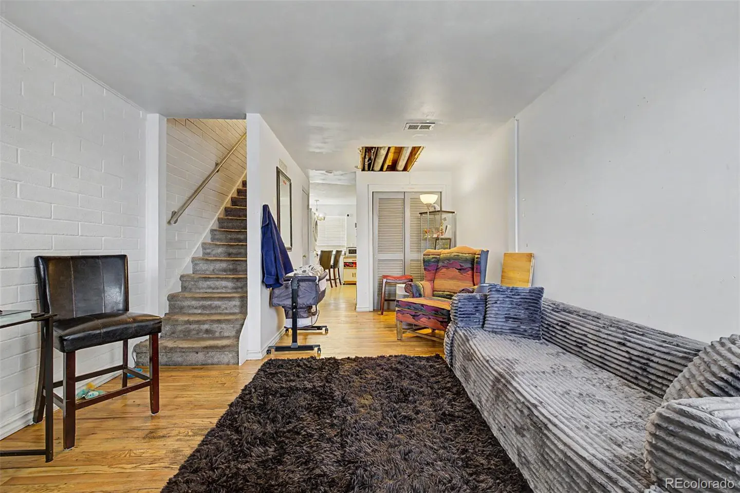 A living room with a gray sofa, a brown shag rug, and a staircase with white brick walls.