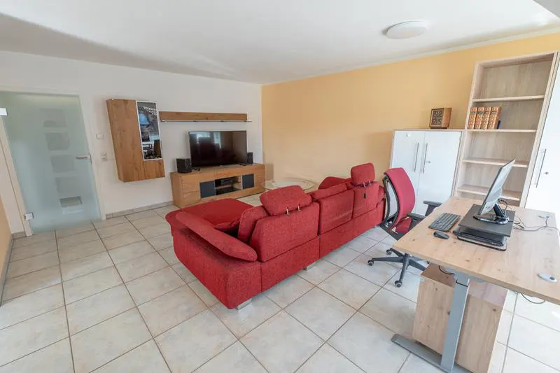 Living room with red sectional sofa, desk with computer, TV, and tile flooring.
