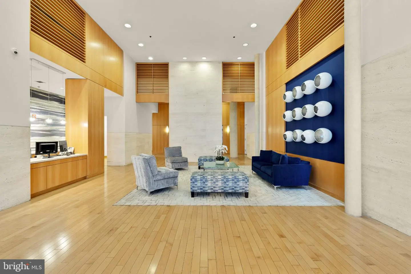Lobby with light wood floors, blue sofa, patterned chairs, and a blue wall with white, egg-shaped art.