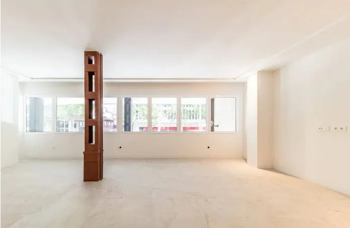 Empty room with white walls, light tile floors, and a decorative brown wooden pillar in front of a row of windows.