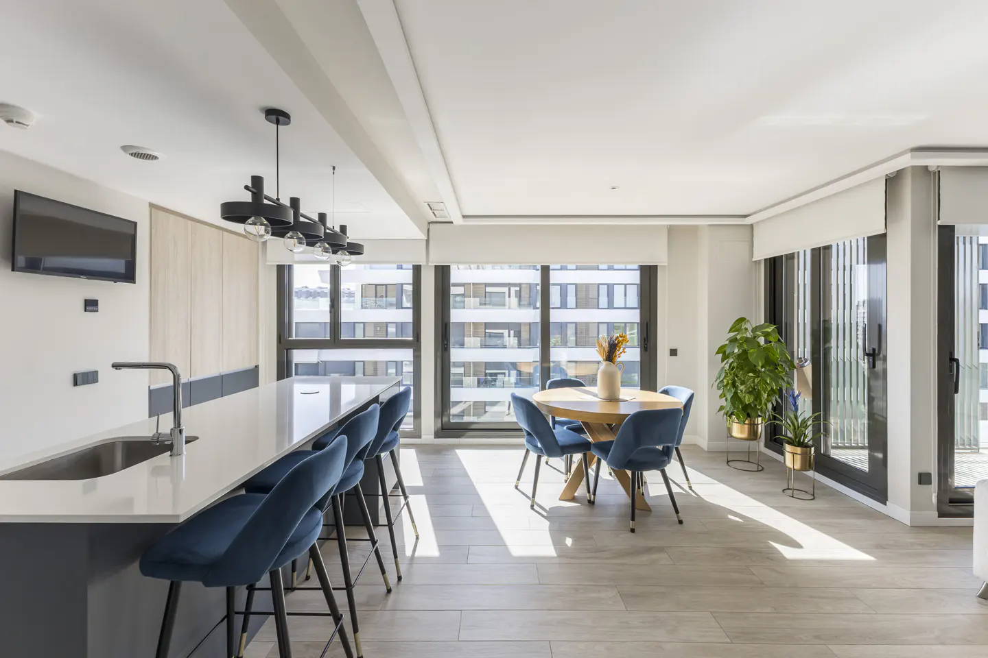 Bright, modern apartment interior with a kitchen island, blue chairs, and a round dining table near large windows.