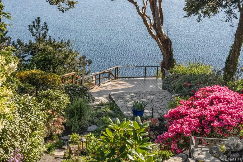 Ocean view from a garden with pink flowers, trees, and a stone patio with wooden railings.