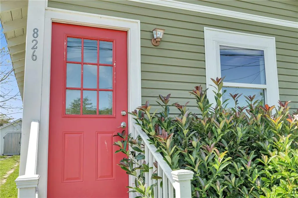 Exterior view of a home with green siding, a red front door with glass panes, and white trim around the door and window. Address number 826 is visible.