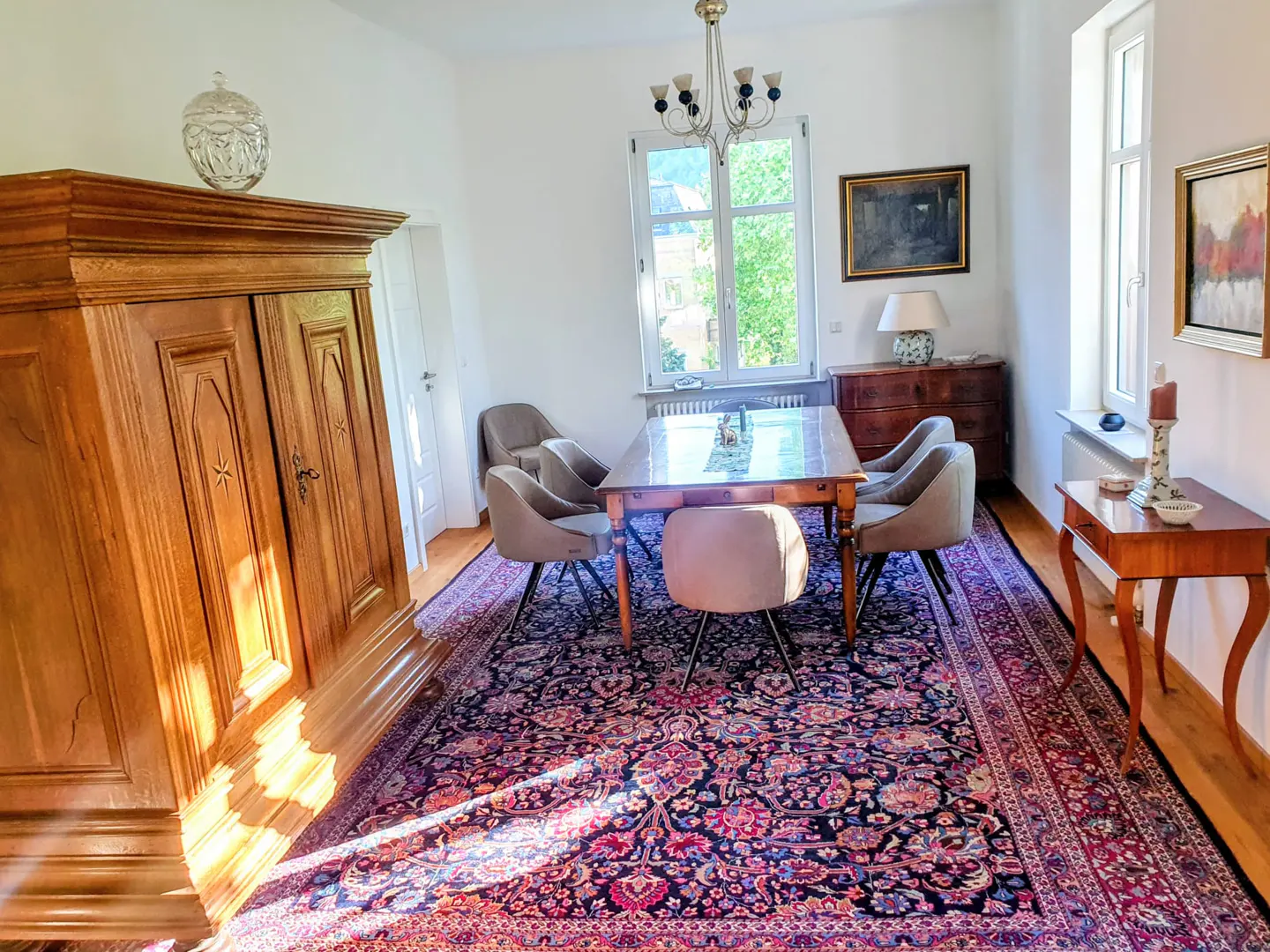 Bright dining room with wood floors, a large oriental rug, a wooden table with six chairs, and a wooden cabinet.