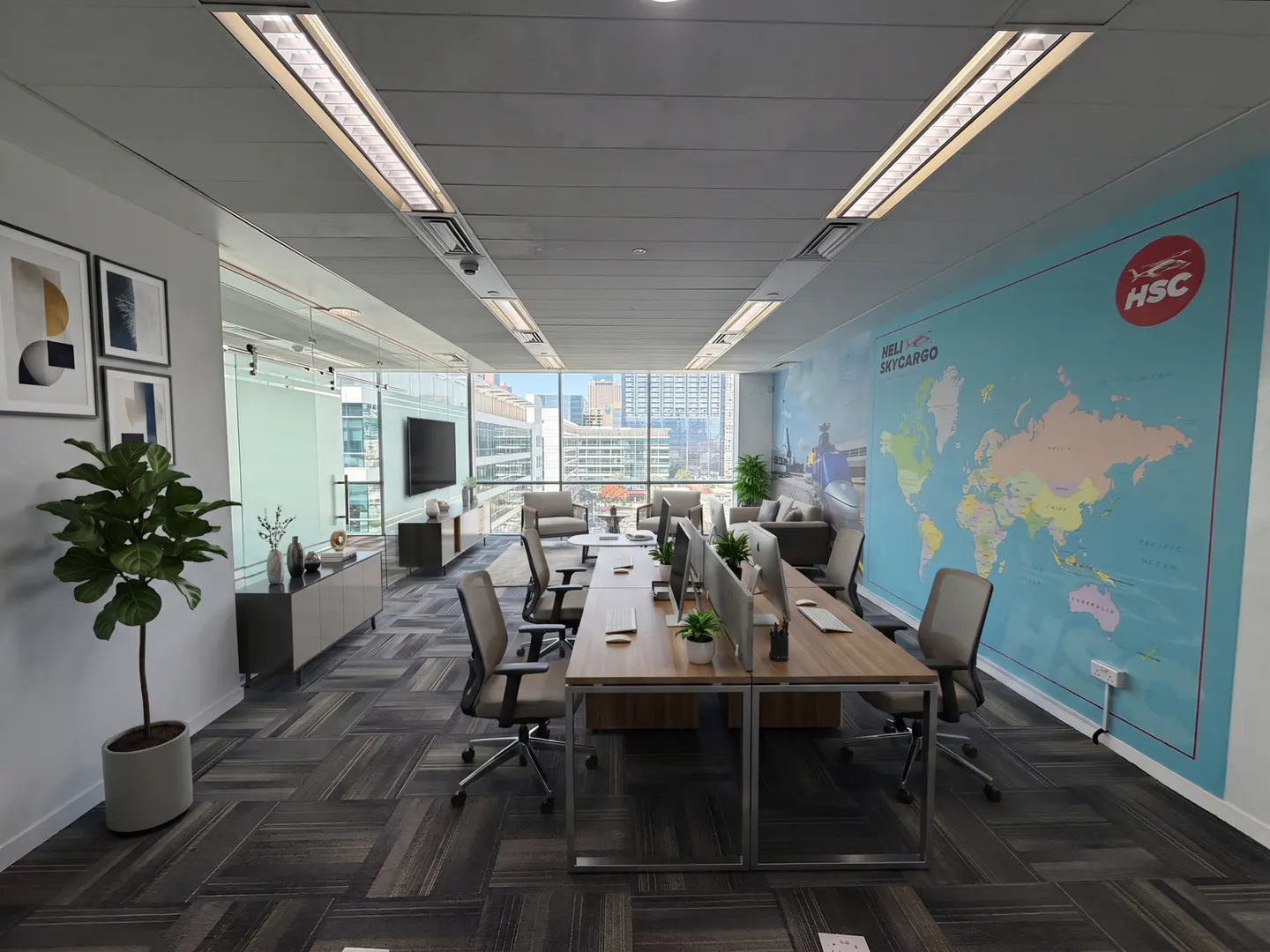Modern office with wooden desks, ergonomic chairs, a large world map mural on the wall, and floor-to-ceiling windows.
