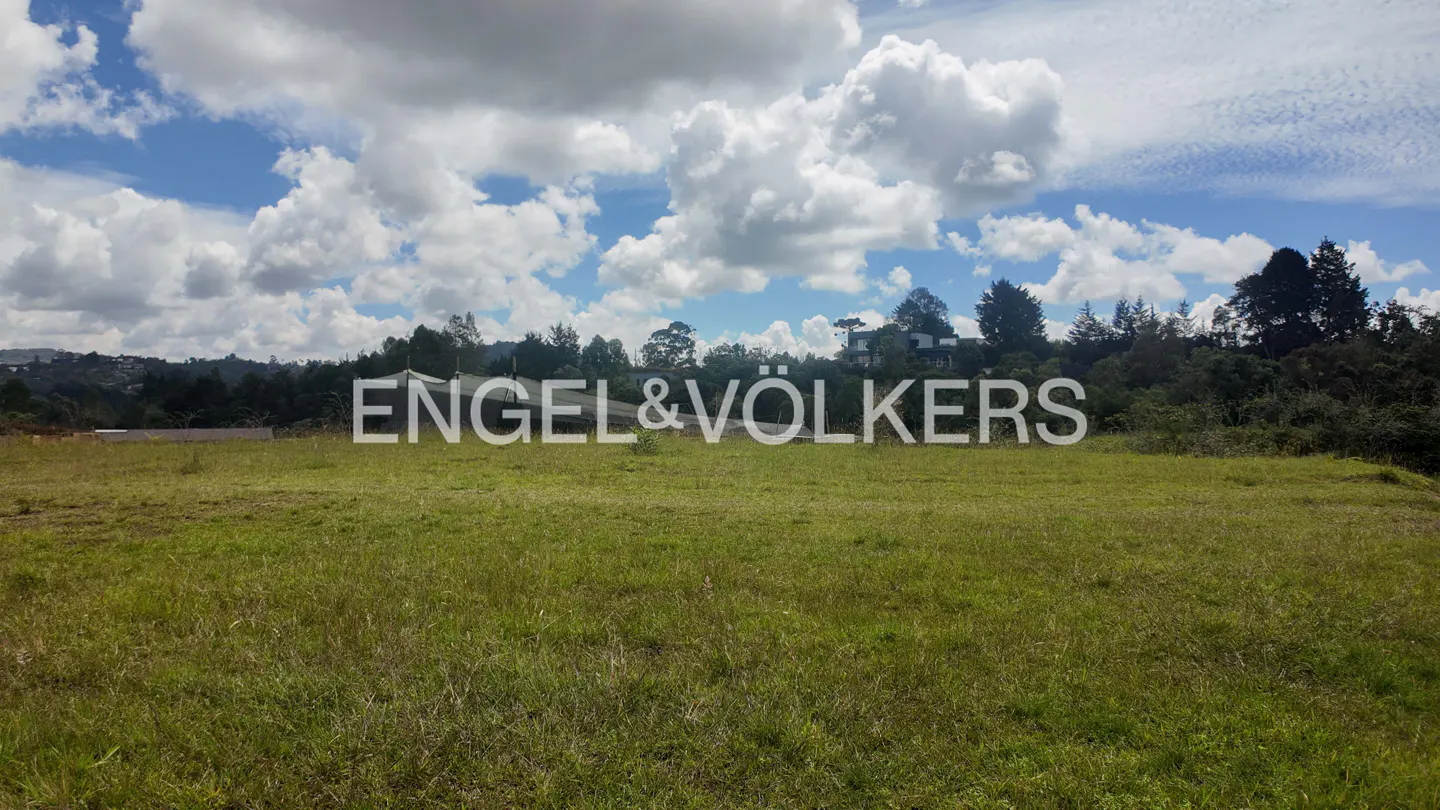 A grassy field with trees and a cloudy sky. The Engel & Volkers logo is superimposed on the image.