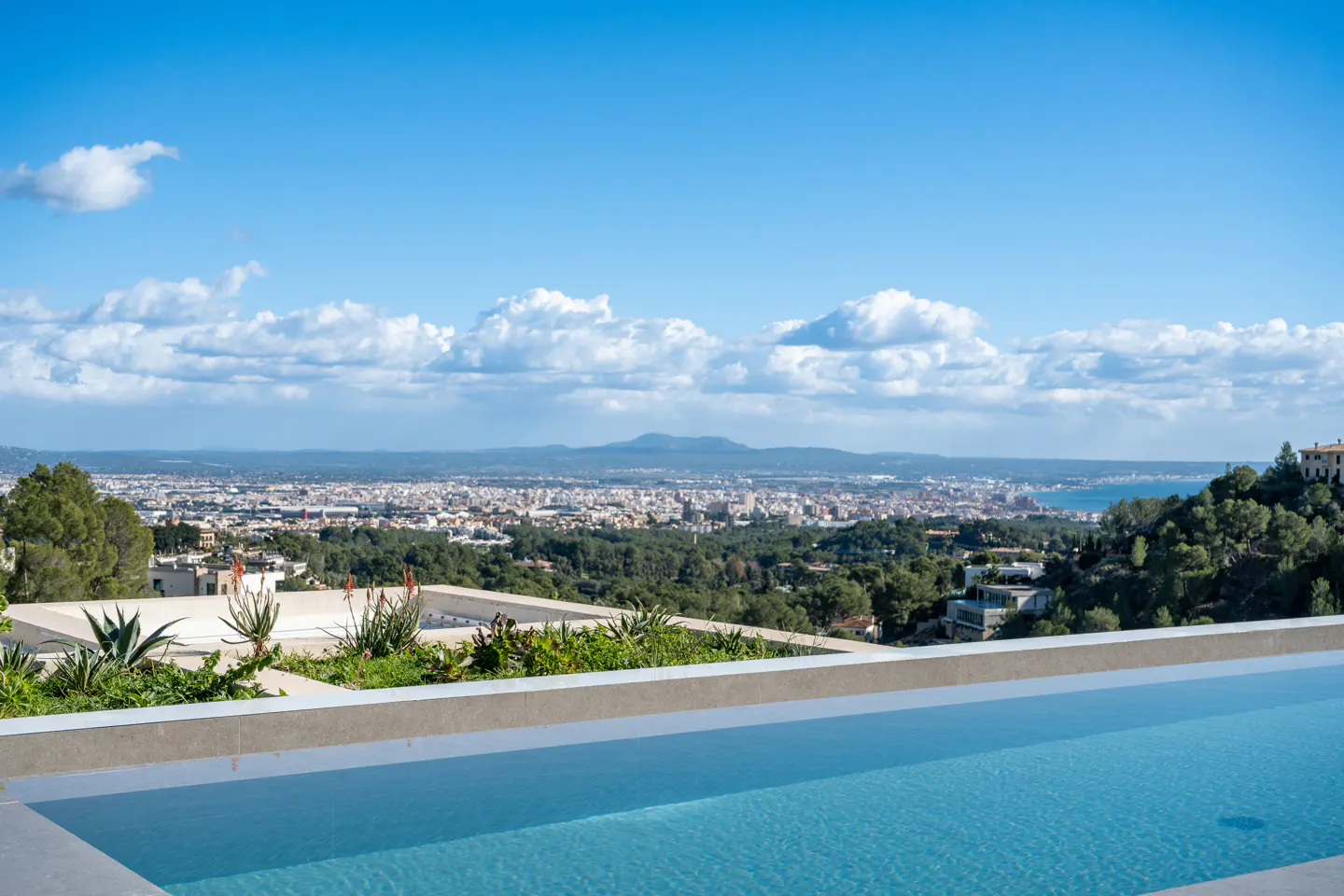 A scenic view from a pool overlooking a city, with a blue sky and scattered clouds above.