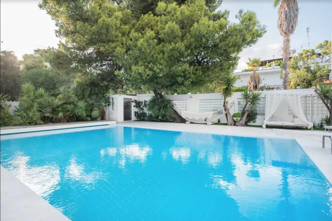 A bright blue swimming pool is surrounded by lush greenery, a hammock, and a white cabana.