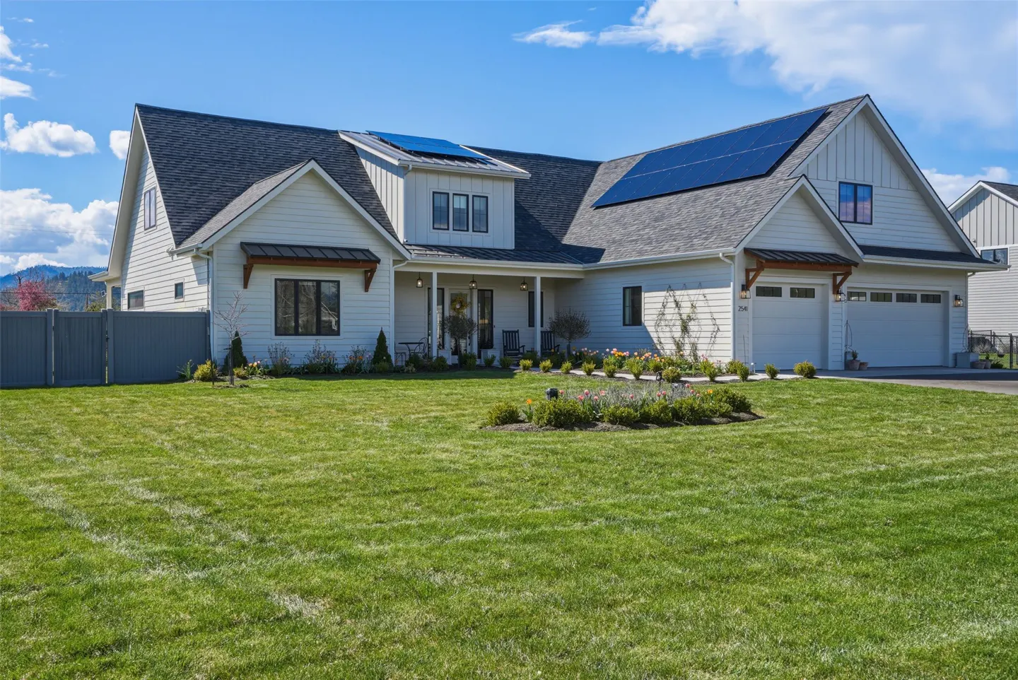 A white, two-story house with solar panels on the roof and a green lawn in front.